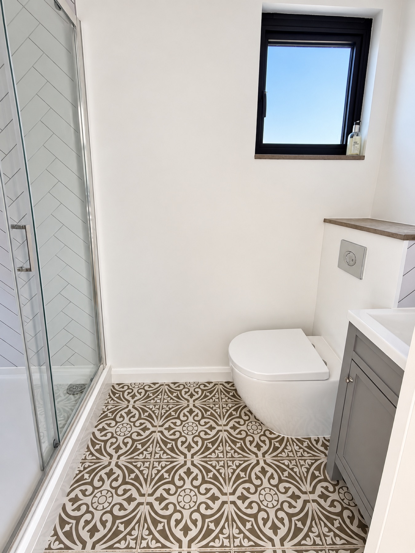 Completed shower room with WC, vanity, shower enclosure and decorative patterned floor tiles
