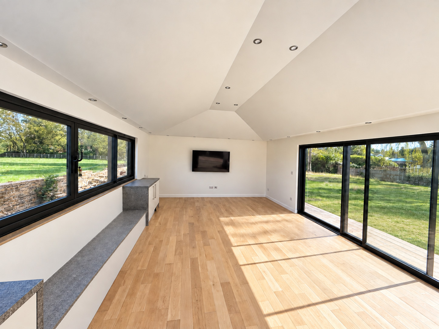 Wide interior view of the finished Maidenhead garden room showing the vaulted ceiling, TV wall, oak floor and garden glazing